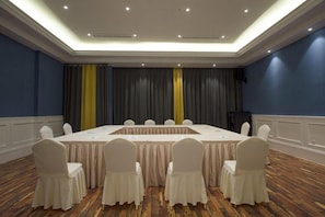 A conference room with a long table, white chairs, and a stage with curtains. - Fanpu Art Hotel (Jiaxing)