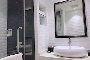 A modern bathroom with a glass shower enclosure, a white sink with a large mirror, and white tiled walls.