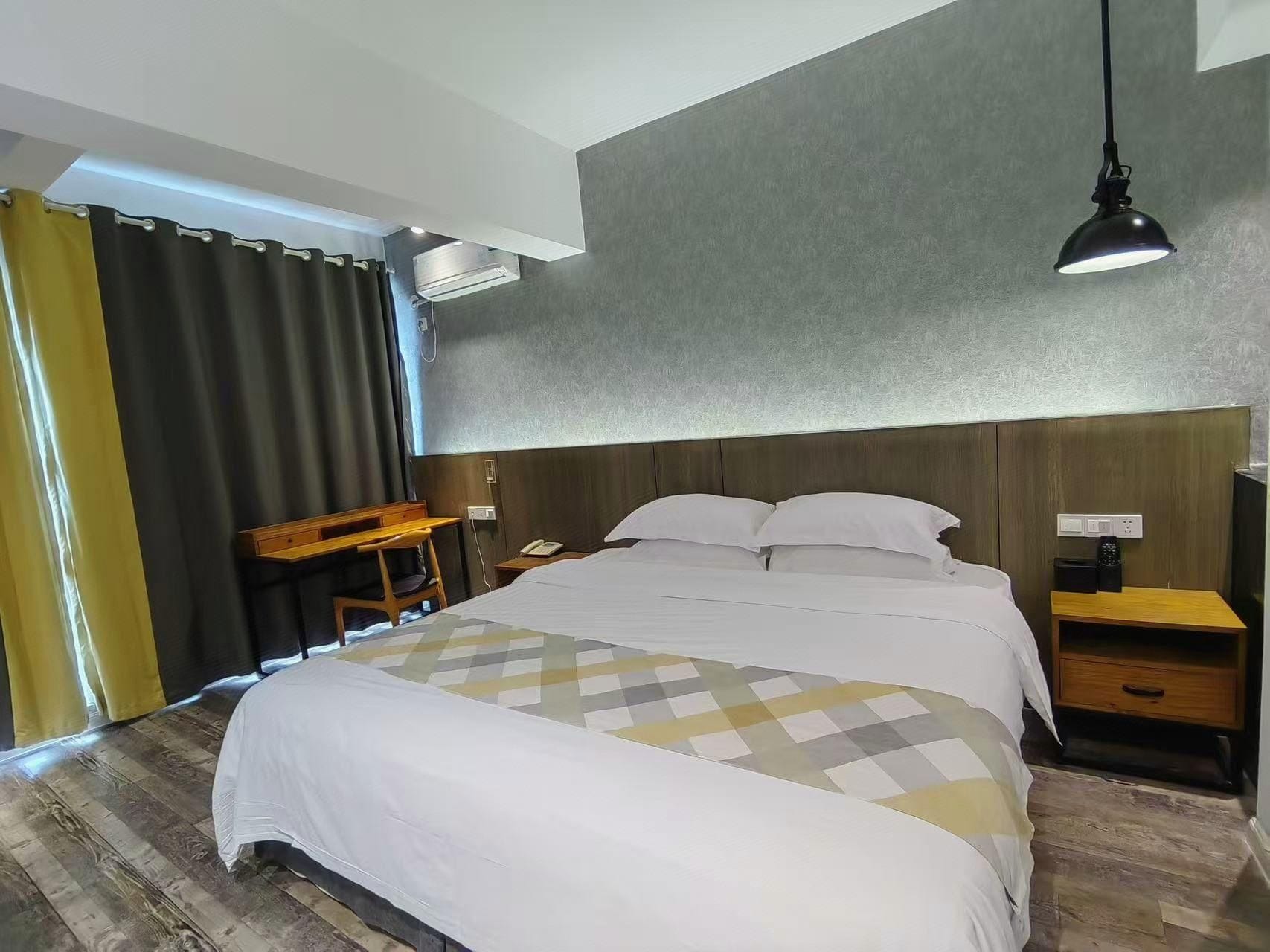 A hotel room with a bed, bedside tables, a desk, and a hanging lamp.
