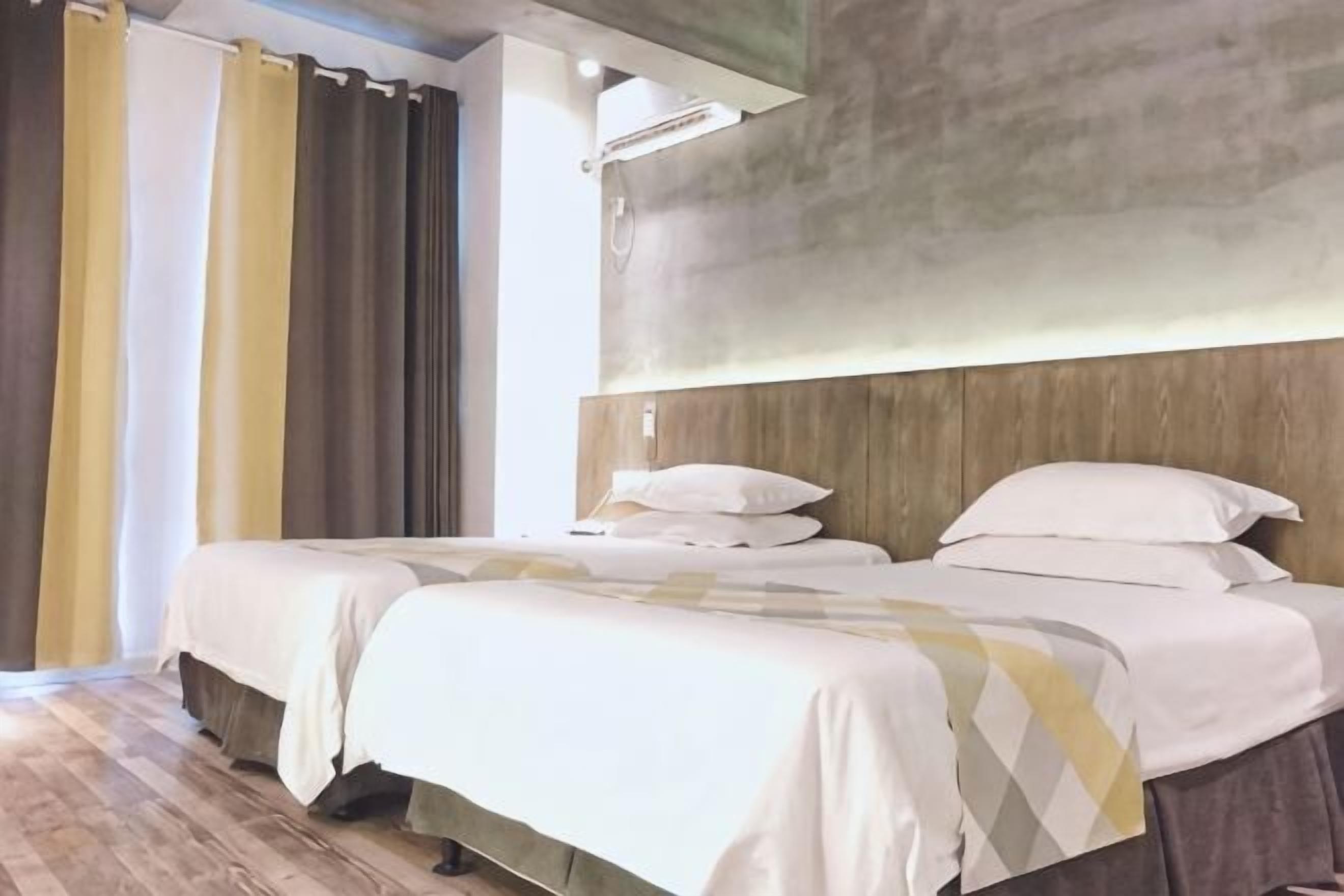 A hotel room with two beds, a wooden headboard, and a large window with curtains.