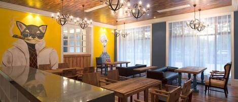 A restaurant interior with wooden flooring, a central bar area, and a mural of a cat on the wall.