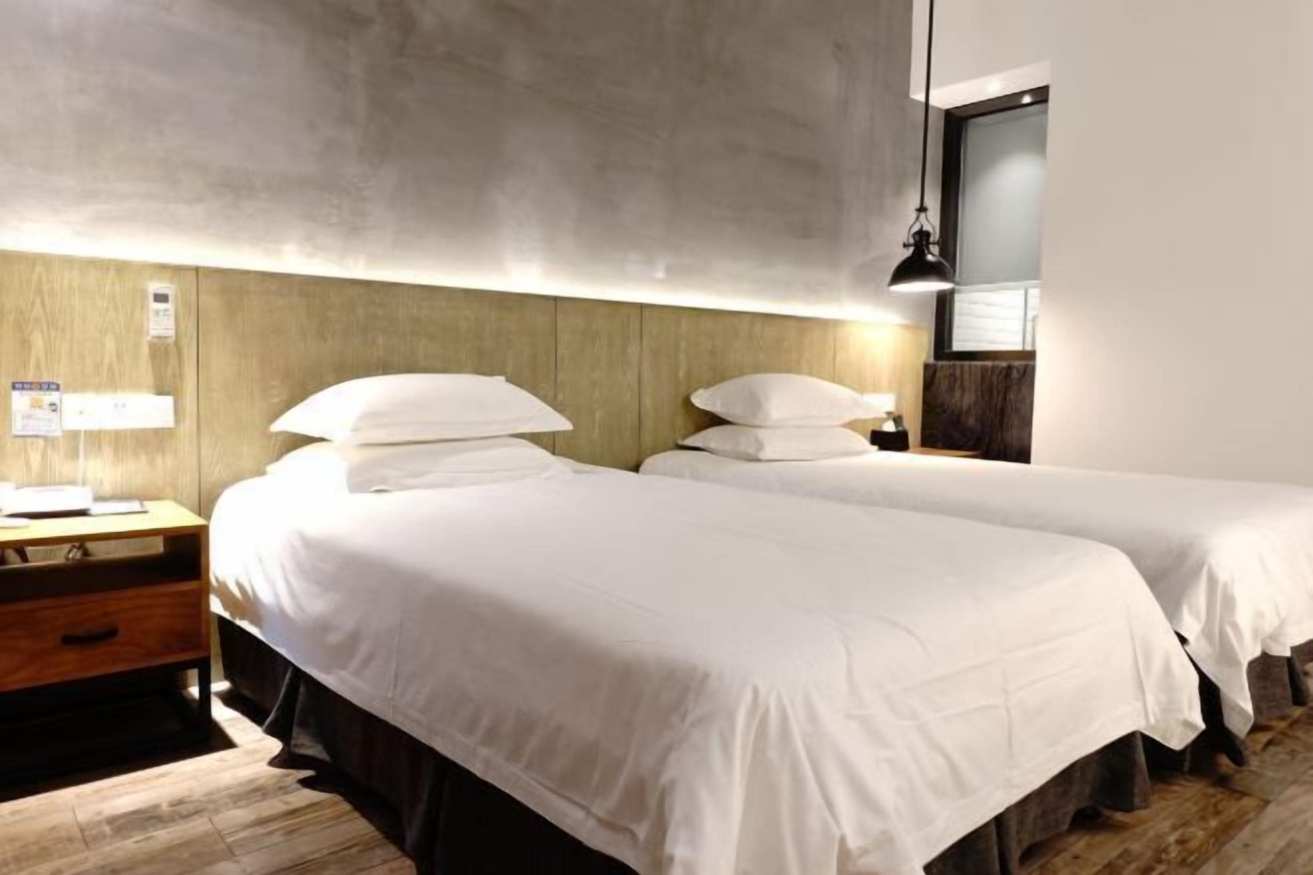 Una habitación de hotel con dos camas, una mesita de noche de madera, un escritorio y una lámpara.