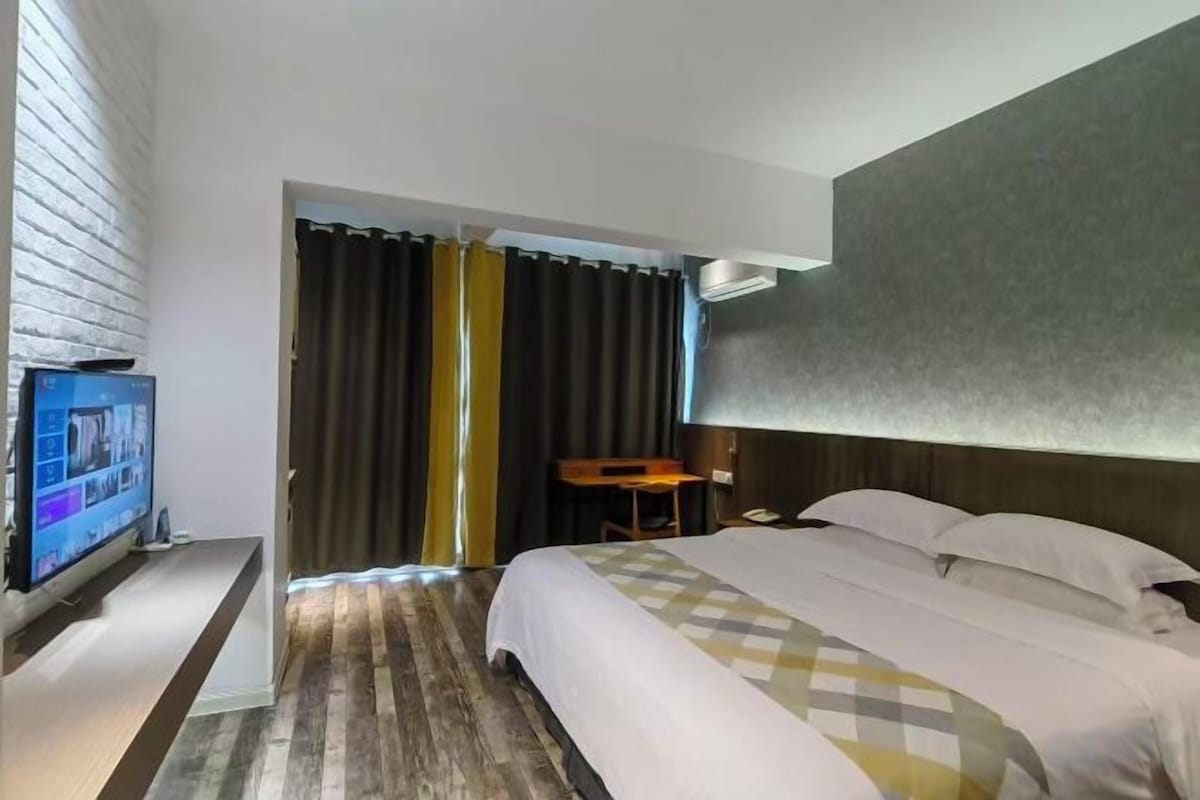 A hotel room with a bed, a television, a desk, and a window with curtains.