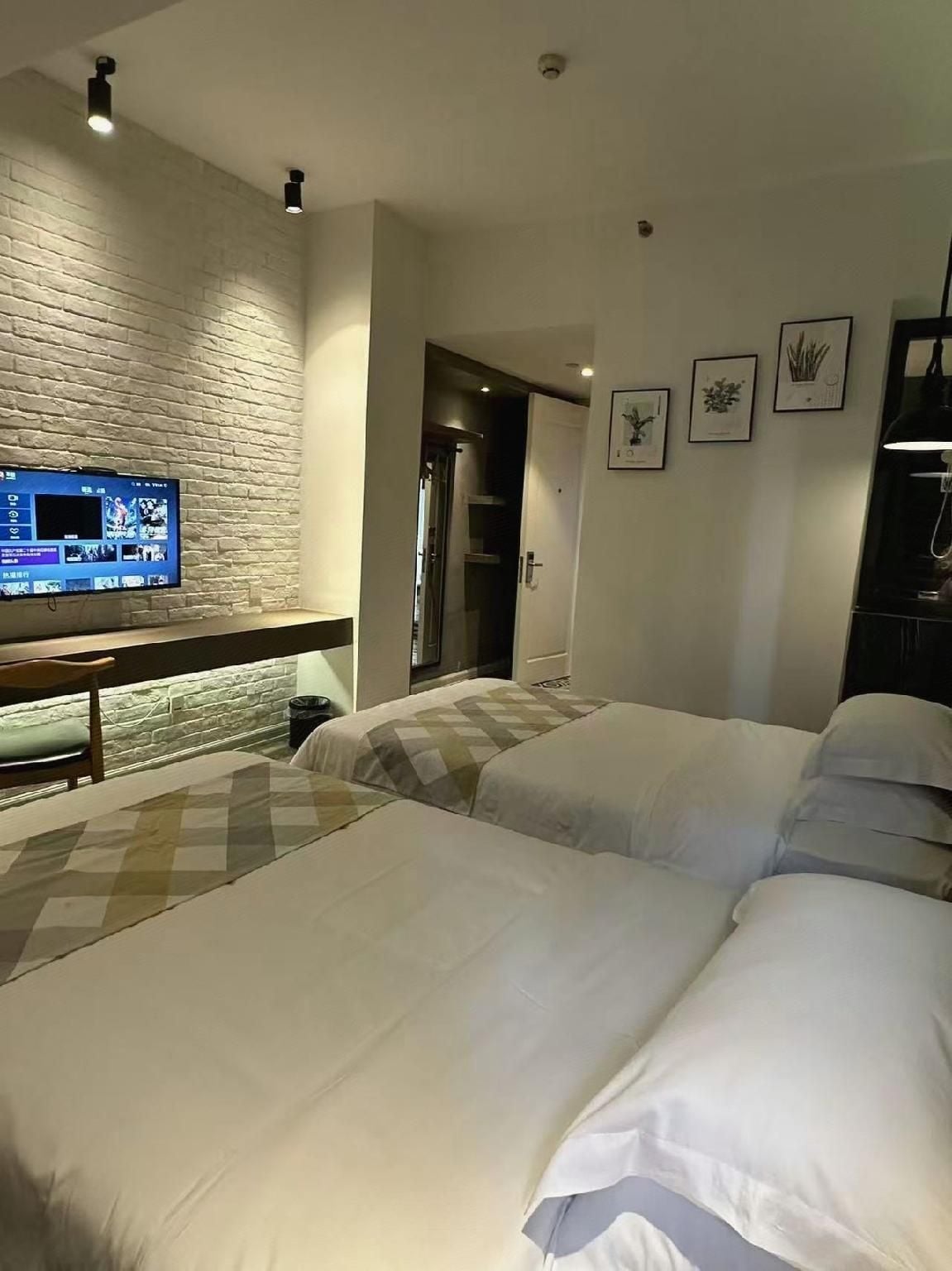 A hotel room with a brick wall, a flat-screen TV, a bed with white bedding, and a door leading to a bathroom.