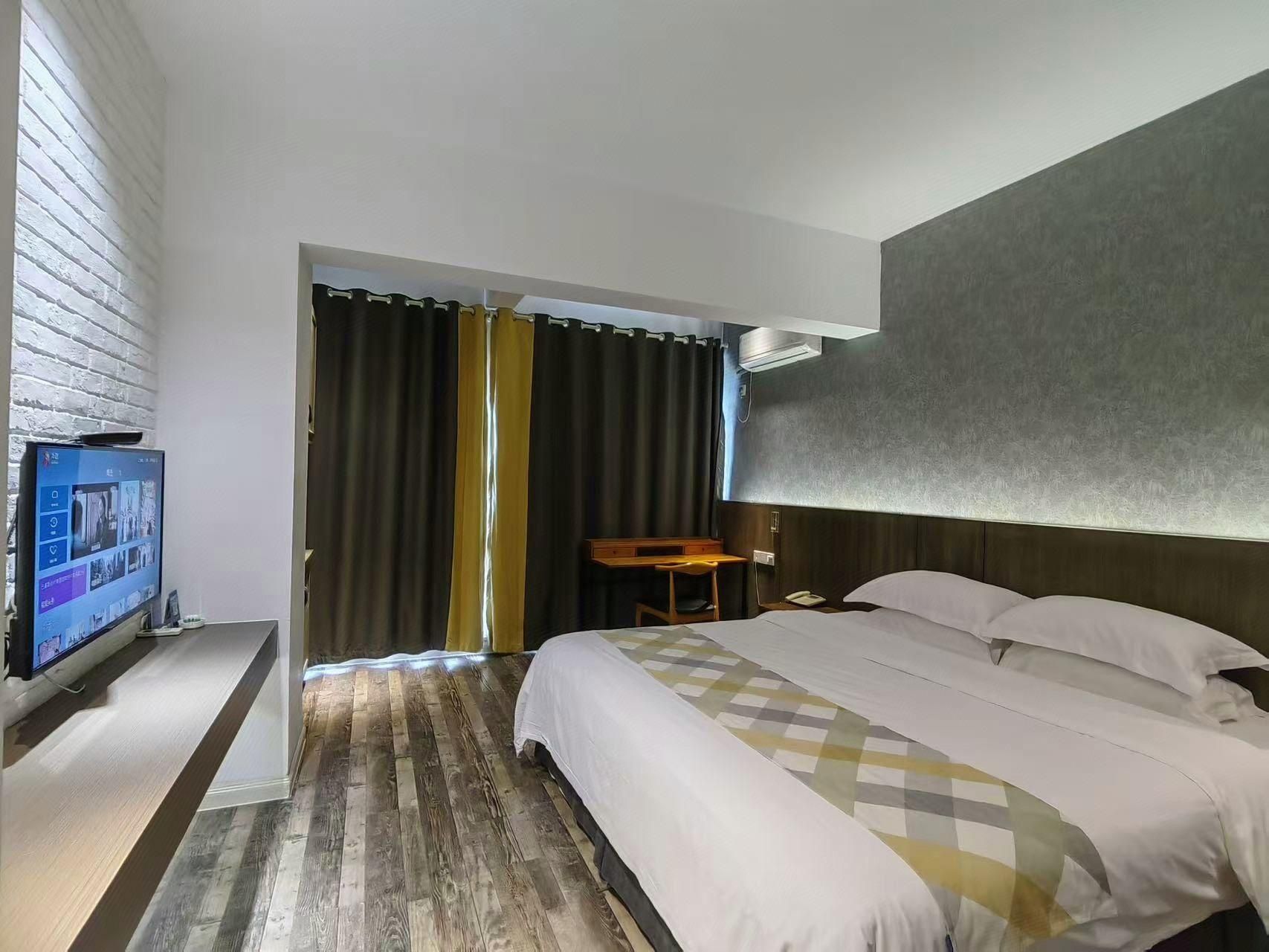 Une chambre d’hôtel avec un lit, un bureau, une télévision et une grande fenêtre avec des rideaux.