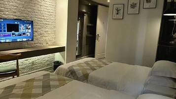 A hotel room with a brick wall, a flat-screen TV, a bed with white bedding, and a door leading to a bathroom.