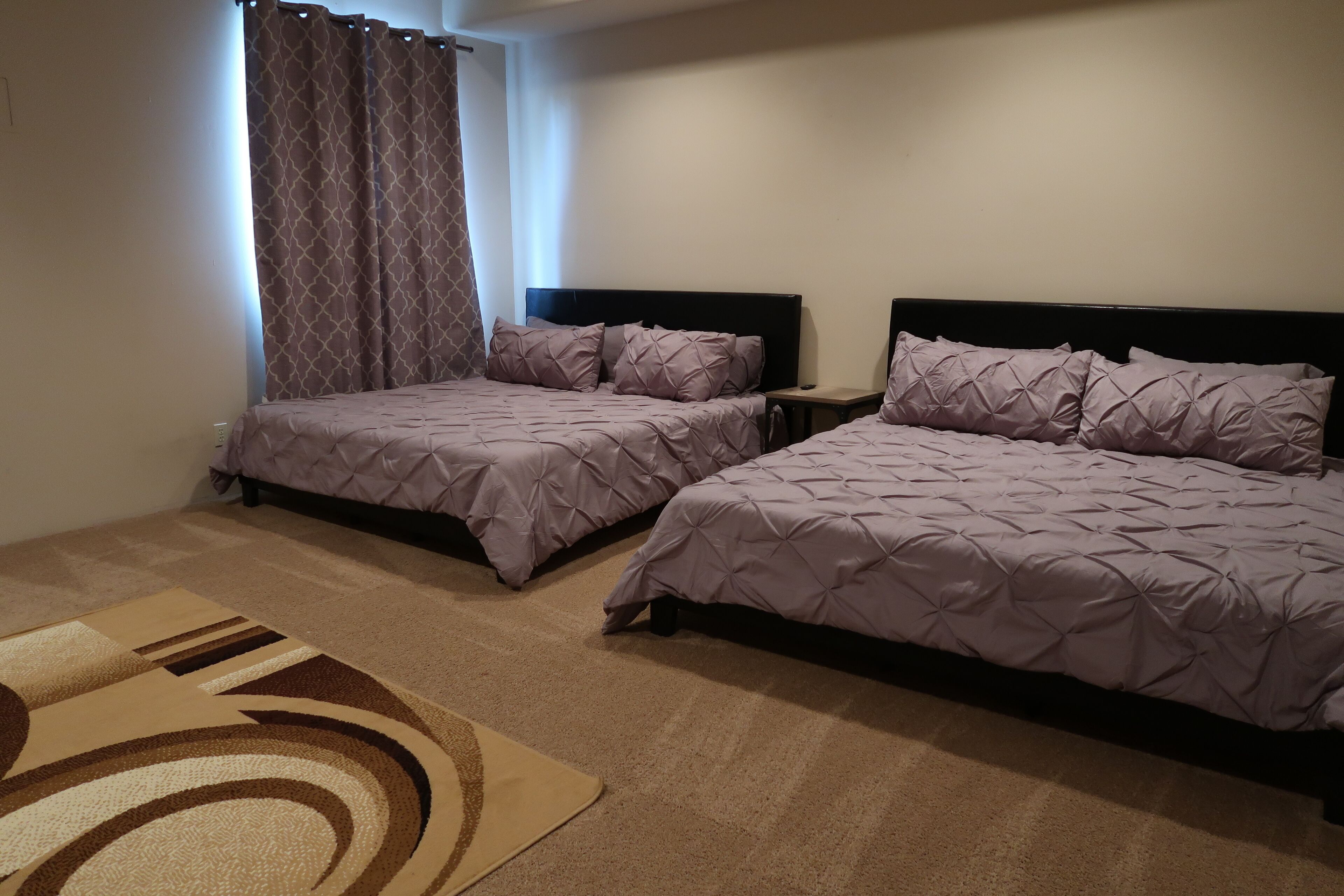 A hotel room with two beds, a small bedside table, a nightstand, and a patterned rug.