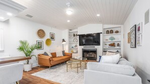 A modern living room with a brown sofa, white armchairs, a TV, and shelves with decorative items. - 5-3 1/2 Aventura-Heated Pool-Gas Grill-Coverd Patio (North Miami Beach)