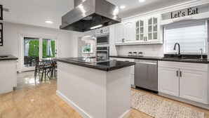 A modern kitchen with white cabinetry, a central island, stainless steel appliances, and a 'Let's Eat' sign. - 5-3 1/2 Aventura-Heated Pool-Gas Grill-Coverd Patio (North Miami Beach)