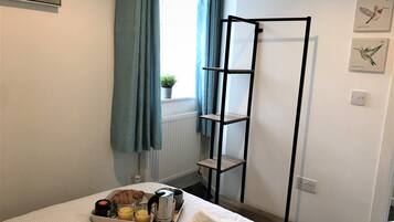 A neatly made bed with a tray of breakfast items, a black metal shelf unit, and a window with blue curtains.