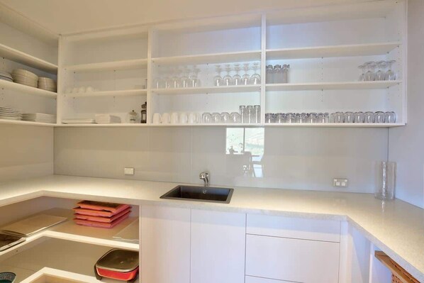 A kitchen with white cabinets, a black sink, and shelves with glassware and plates.