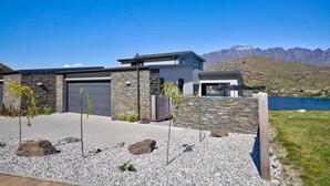 A modern house with a stone facade, a garage, and a view of mountains and a lake. - Ultimate Heights Queenstown Jaw dropping views (Queenstown)