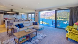 A modern living room with a large sofa, a coffee table, and a view of a mountainous landscape through large windows. - Ultimate Heights Queenstown Jaw dropping views (Queenstown)