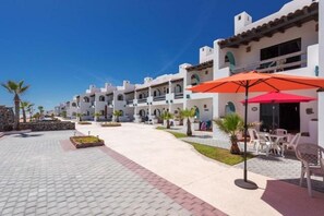 Une cour d’hôtel avec des bâtiments blancs, des espaces de repos en plein air et des palmiers.