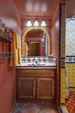 Une salle de bain avec un meuble-lavabo en bois, un pare-feu en carrelage et un miroir surmonté d’un arc décoratif.