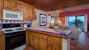 A kitchen with wooden cabinets, a stove, and a microwave. There is a tiled backsplash and a window with a view of the ocean. - Paradise Villa 20 by Kivoya (Puerto Peñasco)