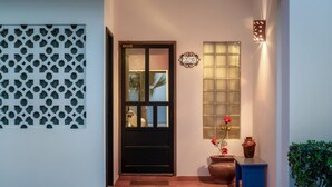 A modern entrance with a black door, a decorative wall panel, a wall-mounted clock, a window with a decorative grille, and a small table with a vase and a potted plant. - Paradise Villa 20 by Kivoya (Puerto Peñasco)
