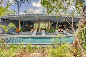 A pool area with lounge chairs, a concrete structure overhead, and surrounding greenery. - Luxury & Nature Meet Plus a Private Pool & Roof Pool (Tulum)