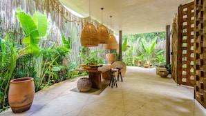 A tropical-themed interior with a dining area, large potted plants, and a wooden partition with shelves. - Luxury & Nature Meet Plus a Private Pool & Roof Pool (Tulum)