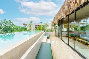 A modern infinity pool with a glass balustrade, a thatched roof, and a view of lush greenery. - Luxury & Nature Meet Plus a Private Pool & Roof Pool (Tulum)