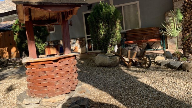 Een terras met een houten pergola, een stenen bankje en een kleine tuin met een palmboom.