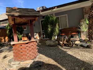 Un patio con un pérgola de madera, un banco de piedra y un pequeño jardín con una palmera.