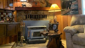 Een gezellige woonkamer met een stenen openhaard, een blauwe houtkachel en een schilderij van een beer aan de muur.