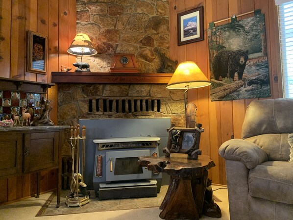 Una sala de estar acogedora con una chimenea de piedra, un estufa de leña azul y un cuadro de un oso en la pared.