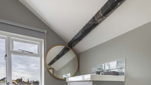 A bathroom with a grey vanity, a round mirror, and a window with a view of buildings. - Sailors Rest (Bideford)