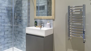 A bathroom with a glass shower enclosure, a sink with toiletries, and a towel rack. - Sailors Rest (Bideford)