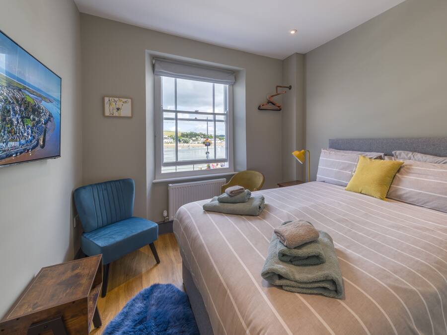 A bedroom with a large bed, a chair, a window, and a painting on the wall.