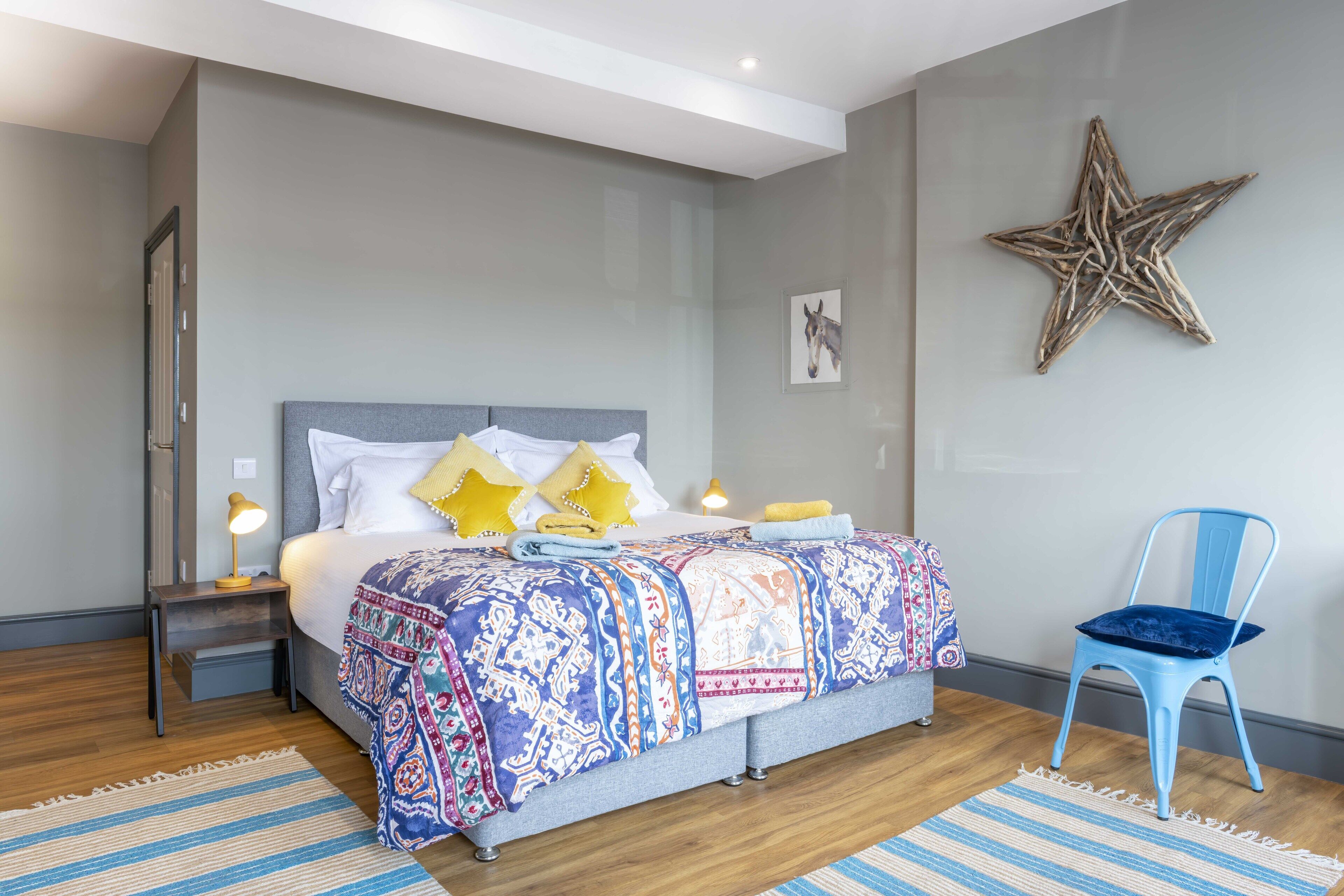 Quarto com cama, mesa de cabeceira, luminária, cadeira, decoração com estrelas e tapete.