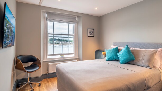 A bedroom with a large bed, a chair, a window with a view, and a framed picture on the wall. - Sailors Rest (Bideford)