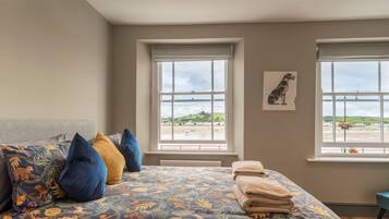 A bedroom with a bed, two windows, a chair, and a painting.