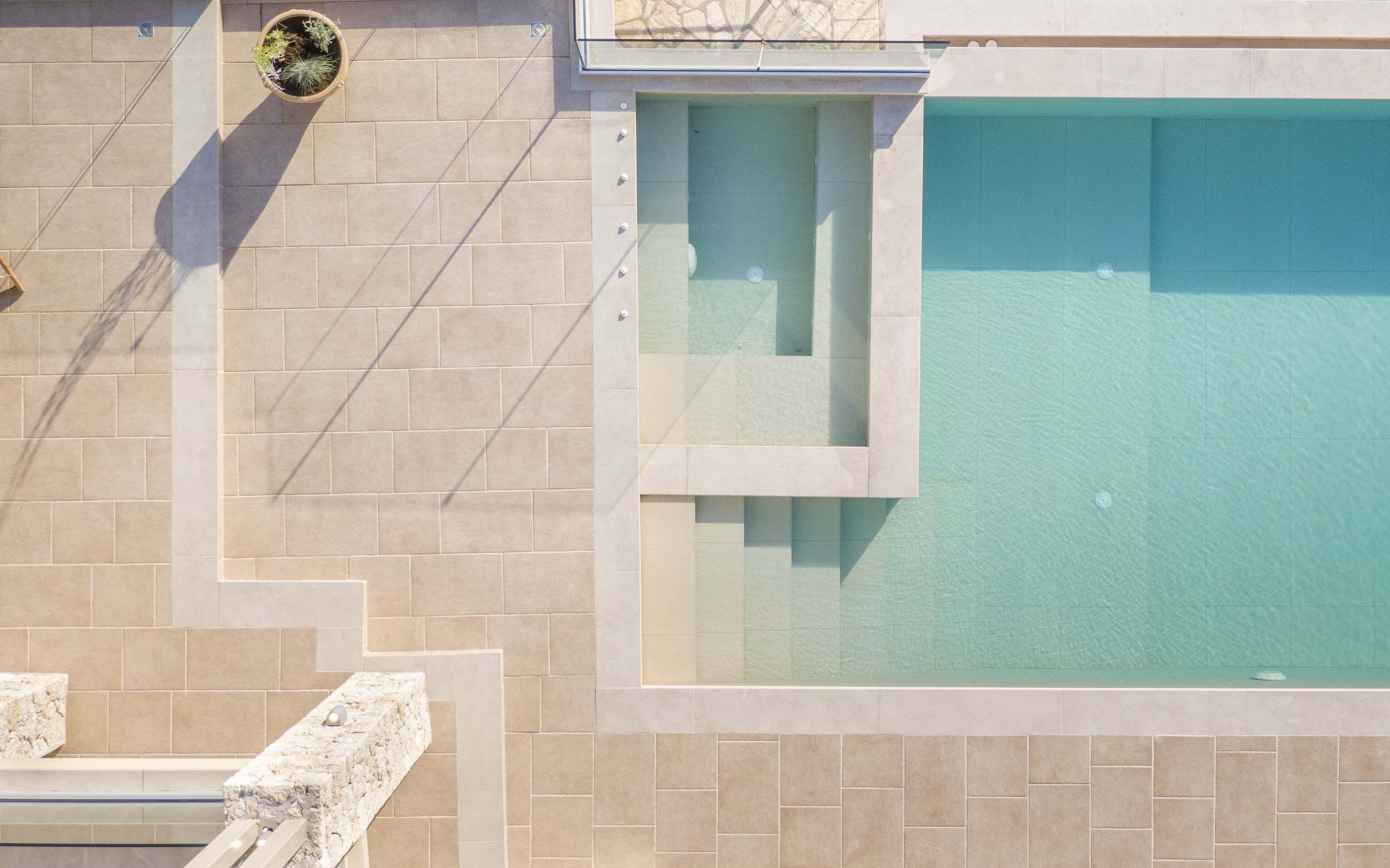 Un espace piscine moderne avec une piscine à l’eau d’un bleu limpide, des murs carrelés et une plante en pot.