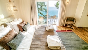 A bedroom with a large bed, a chair, and a view of the sea through a sliding door. - Ocean View - Luxury Villa Ethra (Corfu)