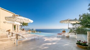 A pool area with a clear view of the sea, outdoor seating, and umbrellas. - Ocean View - Luxury Villa Ethra (Corfu)