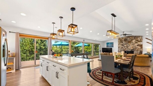 A modern kitchen with a central island, pendant lighting, and a dining area with a stone accent wall. - Serene Tahoe Escape | HotTub | Arcade | EV Charger (South Lake Tahoe)