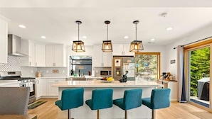 A modern kitchen with white cabinets, a central island with bar stools, and pendant lighting. - Serene Tahoe Escape | HotTub | Arcade | EV Charger (South Lake Tahoe)