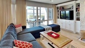 A modern living room with a sectional sofa, a coffee table, and a TV in a white cabinet. - Luxury Condo with Outdoor Dining and Community Pool. (Ponte Vedra)