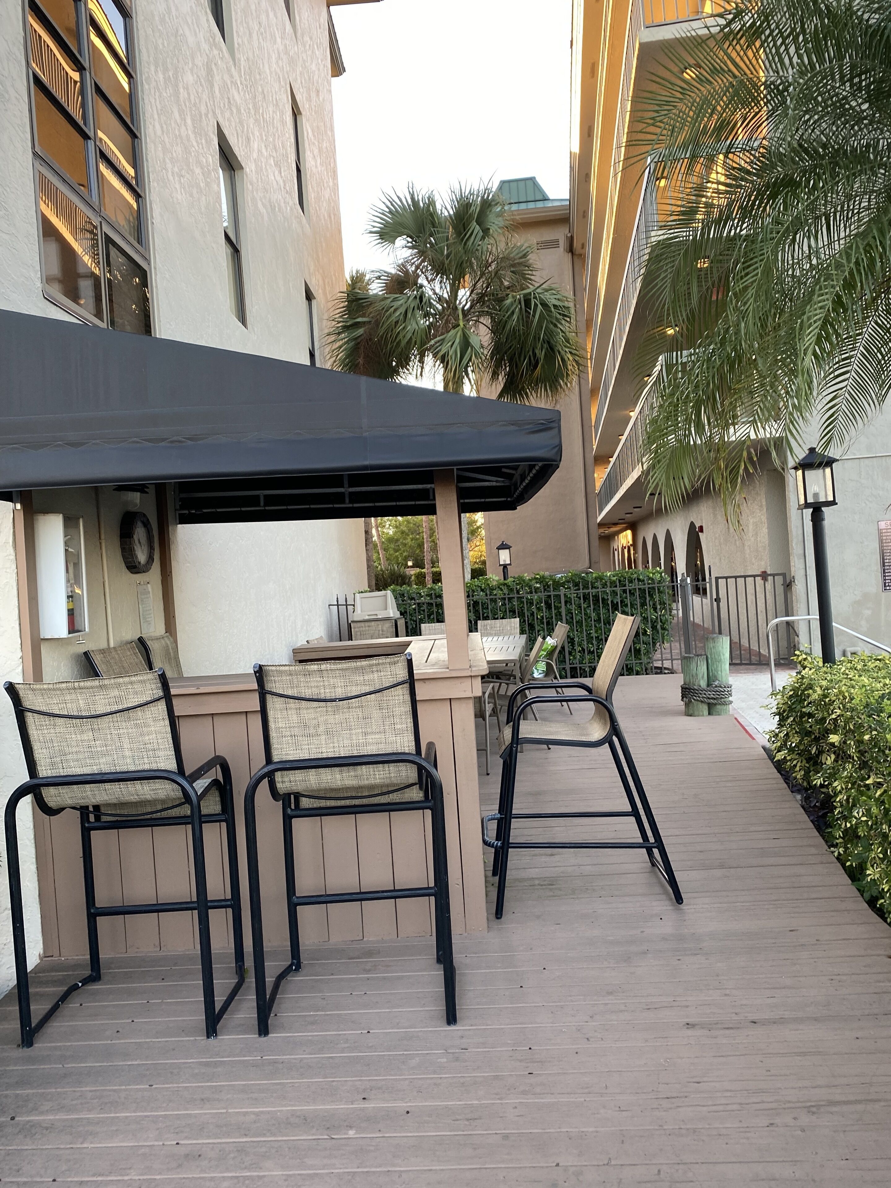 An outdoor seating area with chairs and a table, a covered patio, and a building with balconies and a palm tree.