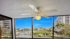 A balcony with a table and chairs, a ceiling fan, and a view of a river and buildings. - Vanderbilt Beach area with Bay views from Lanai. (Naples)