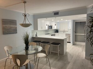 Une cuisine moderne avec des meubles blancs, un îlot central et un coin repas comprenant une table et des chaises en verre.