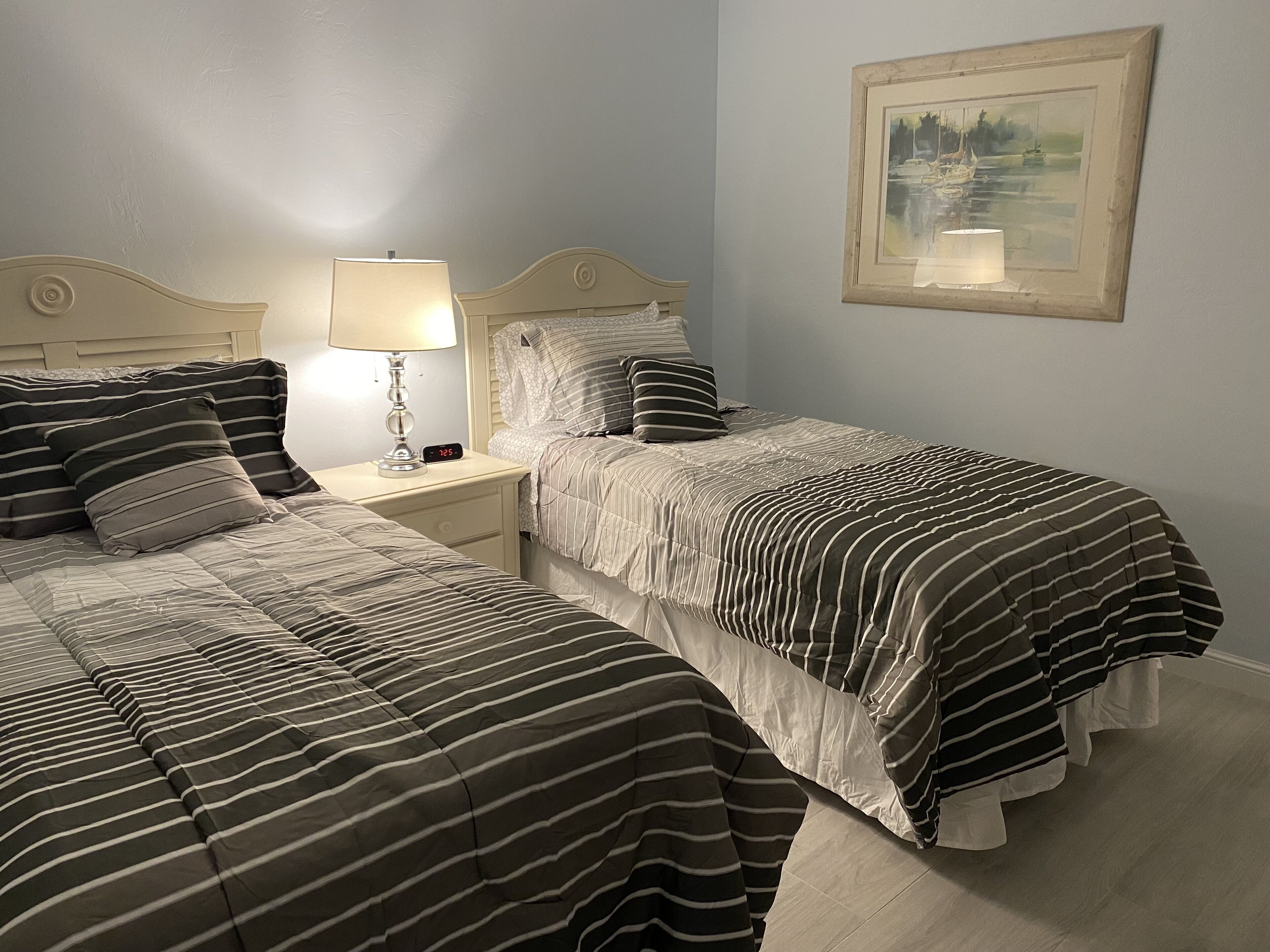 A bedroom with two beds, a nightstand with a lamp, and a framed painting on the wall.
