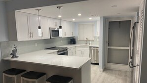 A modern kitchen with white cabinets, a large island with bar stools, stainless steel appliances, and pendant lighting. - Vanderbilt Beach area with Bay views from Lanai. (Naples)