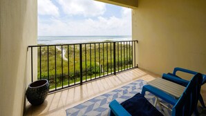 Un balcon avec vue sur l’océan, une plante en pot et des meubles bleus et blancs.