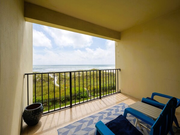 A balcony with a view of the ocean, a potted plant, and blue and white furniture. - Sunkissed Escape | Couple’s Paradise: Oceanfront, Views + Direct Beach Access (Jacksonville Beach)