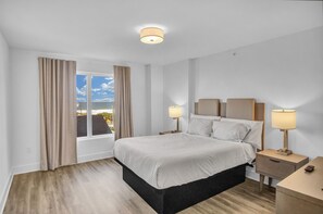 A hotel room with a large bed, two bedside tables with lamps, a window with curtains, and a view of the sea. - Beach Front Condo at the Avalon Club (Clearwater)