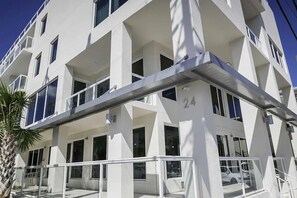A modern multi-story building with balconies, large windows, and a visible car parked in the driveway. - Beach Front Condo at the Avalon Club (Clearwater)