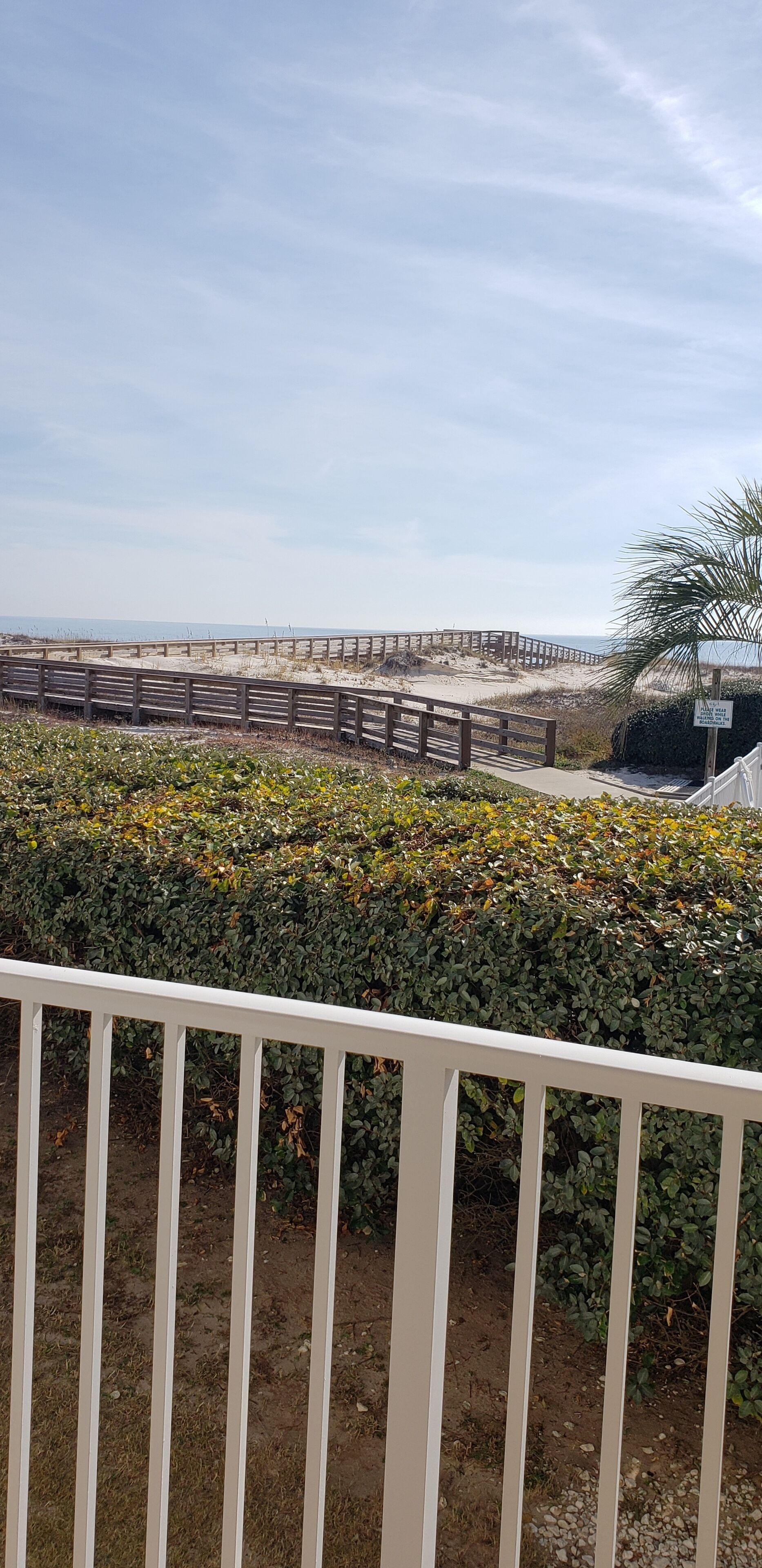 A beach view with a wooden walkway and a white railing in the foreground.